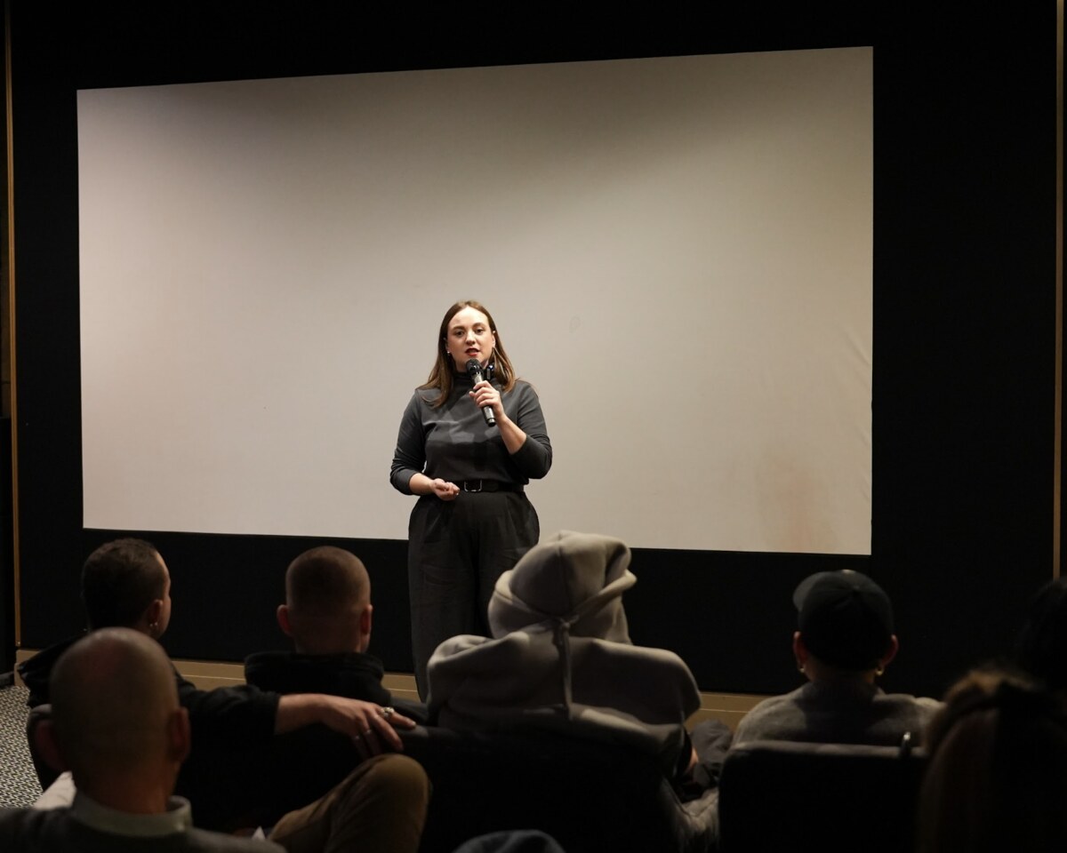 A founder speaking with a microphone to a seated audience in a screening room